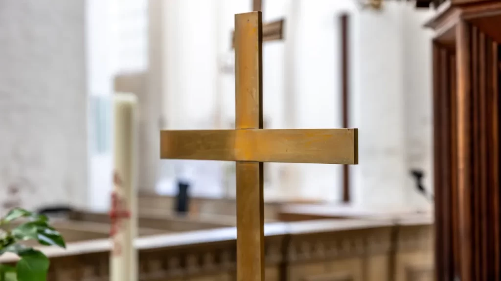 Cruz dourada em capela religiosa preparada para cerimônia de despedida e homenagem póstuma.